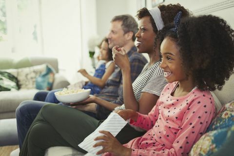 Ung multietnisk familie, der ser film og spiser popcorn på sofaen