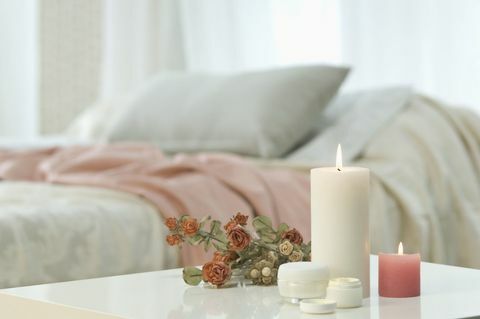 Stearinlys, hudcreme og bundt af roser på bordet med sengen