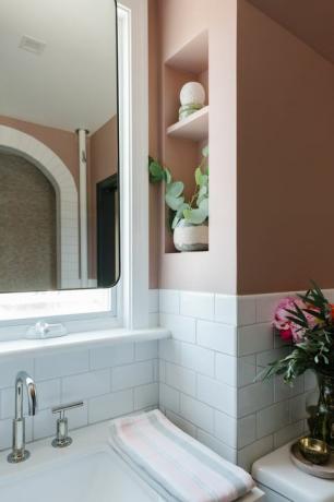 hvide undergrundsfliser, lyserøde malede vægge, sølvhane, spejl, indbyggede reoler, lyserøde og grå håndklæder
