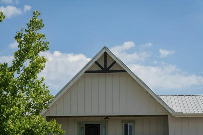 destin, florida cottage tagtop med hvid tavle og lægtebeklædning og sorte trim der er et træ forrest i hytten med en himmel baggrund