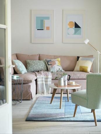 en hvid stue, med en lys pink sofa, et lille rundt sofabord, et blåt tæppe, en grøn stol og et maleri på væggen