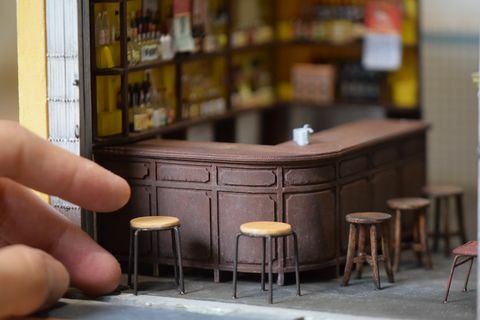 nærbillede af en miniature replika af en bar med barstole og en menneskelig hånd til skala