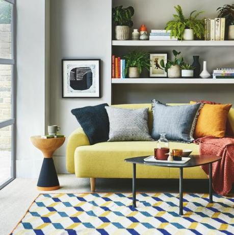 stue, gul sofa hvid hylde bag med et blå og gult mønstret tæppe på gulvet