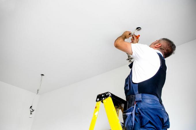 en reparatør en mandlig elektriker monterer lyset og installerer led lys i loftsarmaturen