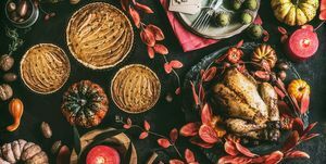 Thanksgiving middagsbord med stegt hel kylling eller lille kalkun, græskartærte på mørk rustik baggrund med tallerkener, sauce, bestik, borddækningsmærker, brændende stearinlys, røde efterårsblade, nødder og festlig dekoration, ovenfra, stilleben, flad lægge