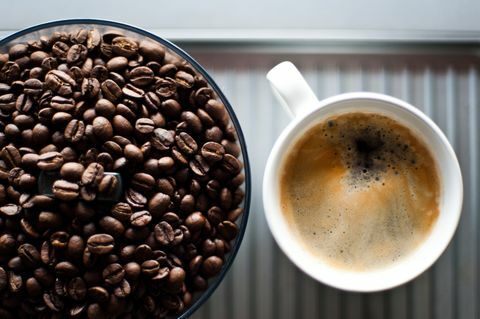 Friske kaffebønner i en kværne foruden en kop frisk sort kaffe