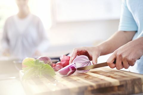 Kvinde skiver rødløg på skærebræt i køkkenet